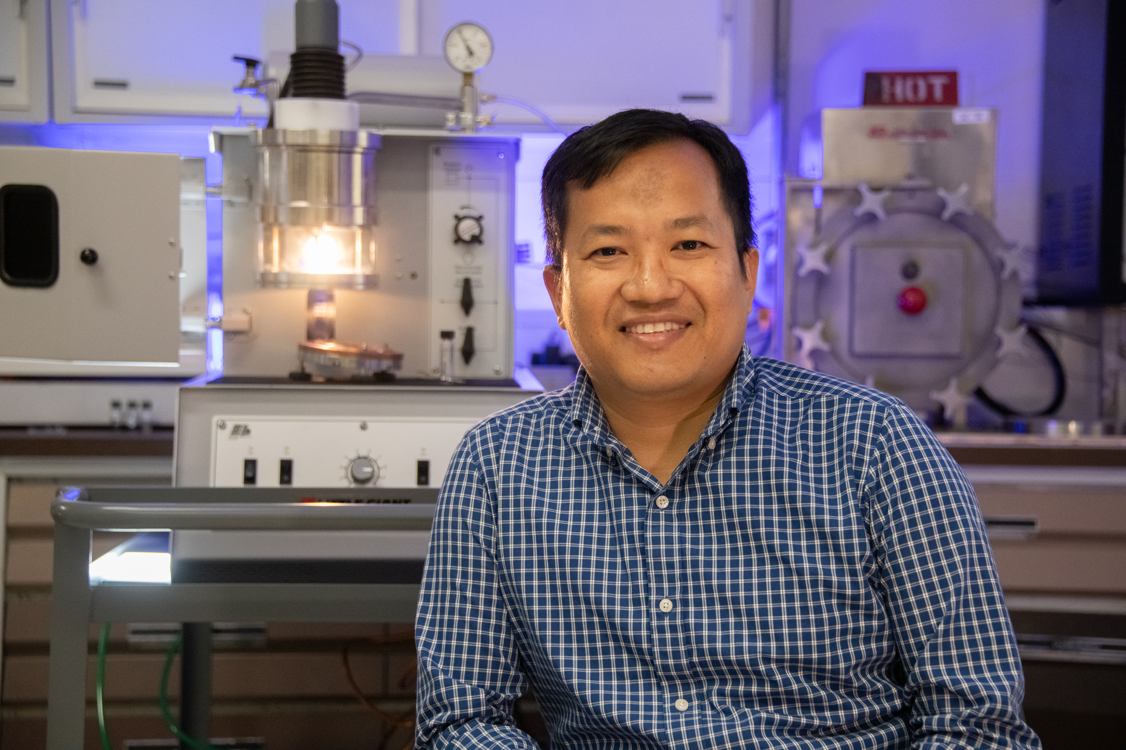 A scientist smiling and sitting in front of lab equipment.