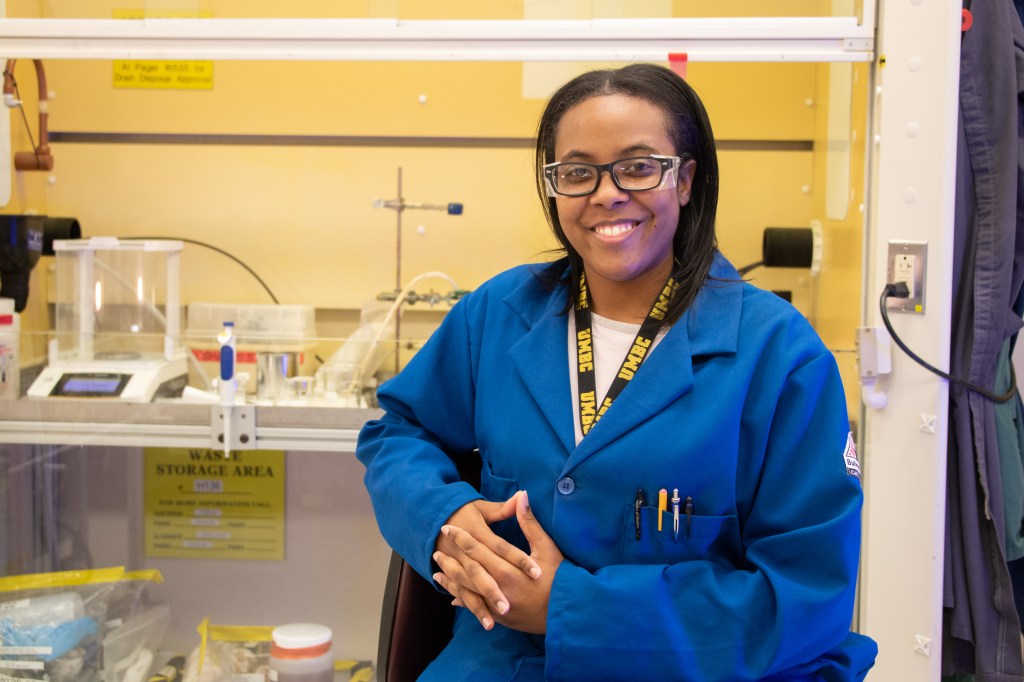 A woman smiling and sitting in a lab.