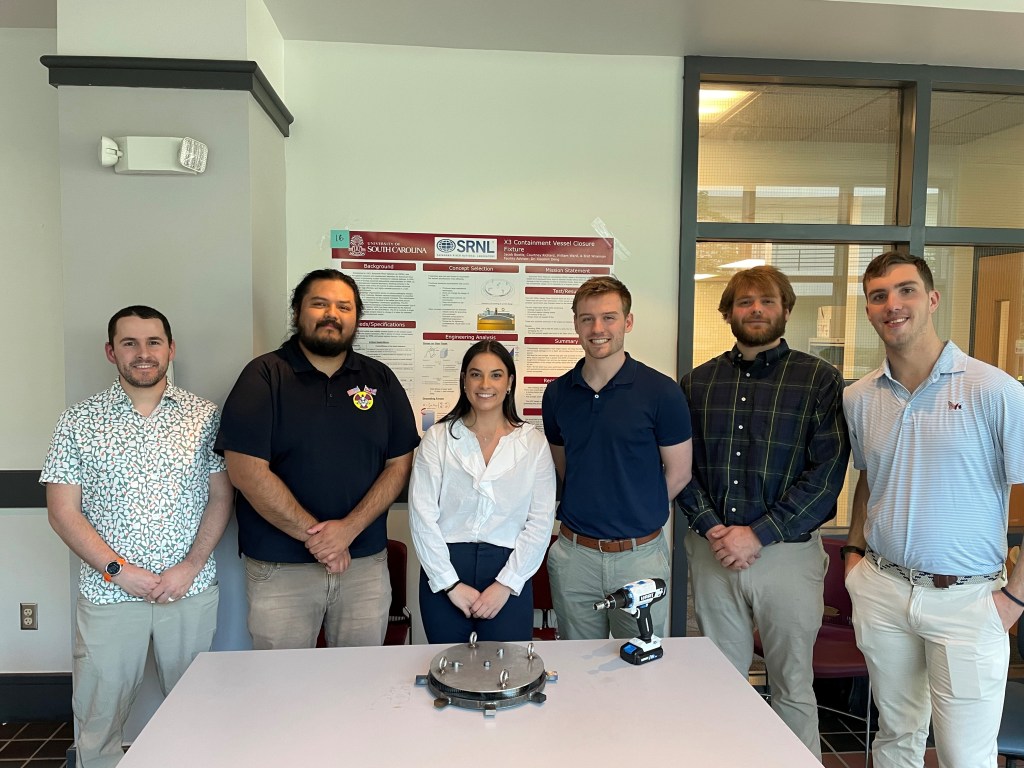A group of students smiling and standing around a table.