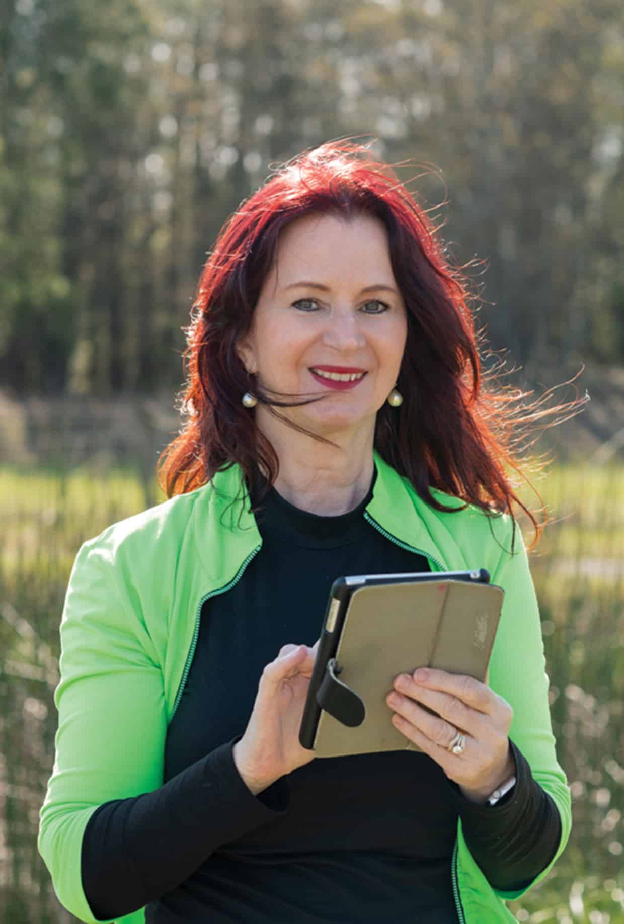 A woman outside smiling, holding a tablet