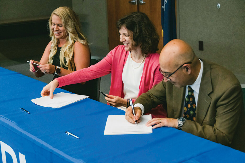 Three people sitting at a table, smiling, signing documents