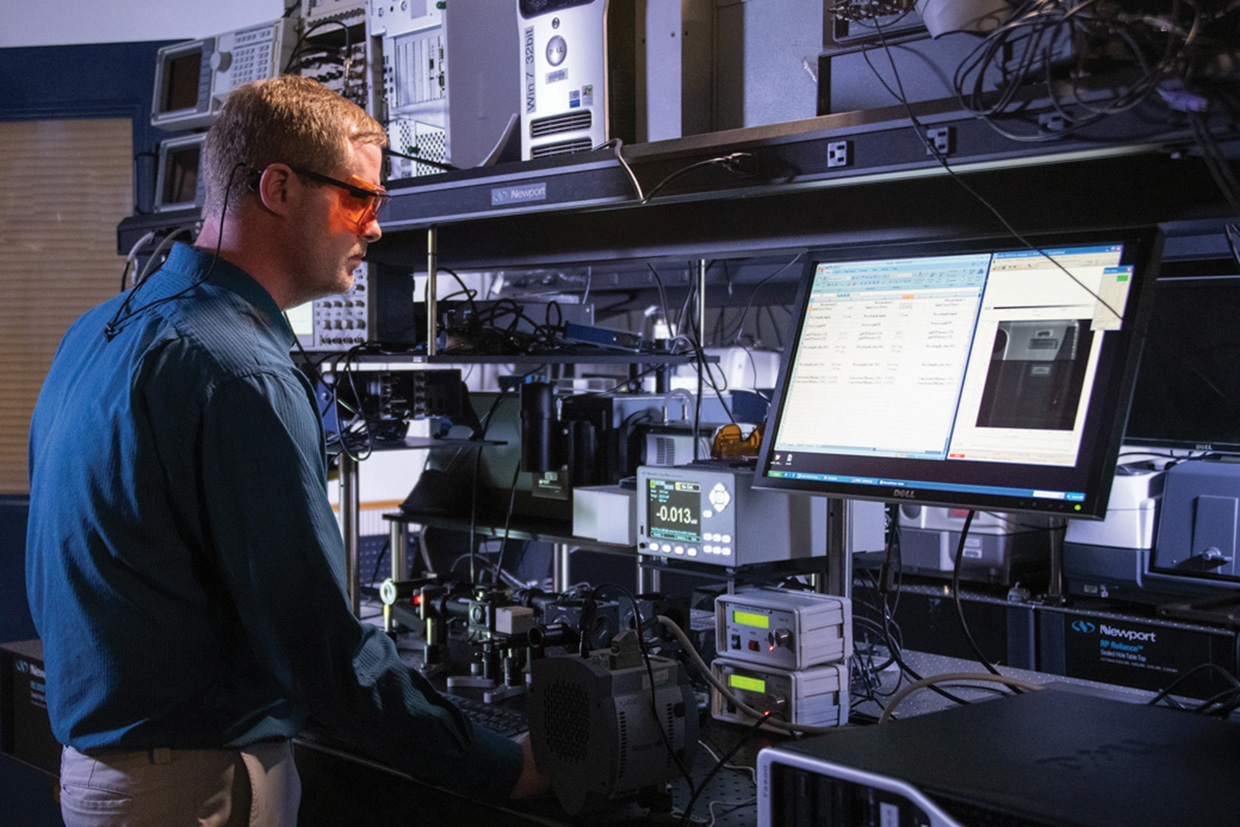 A man wearing safety glasses, working on a computer