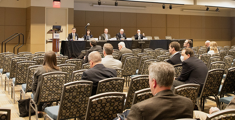 conference room with several attending listening to a panel of people