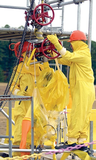 Two men in safety suits guiding a tube through waste tanks