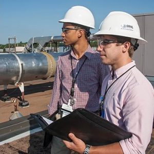 Two male interns with hardhats standing on roof of building looking towards project site