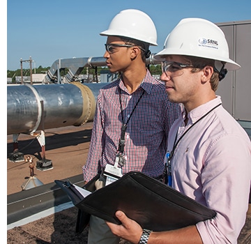 Two male interns with hardhats standing on roof of building looking towards project site