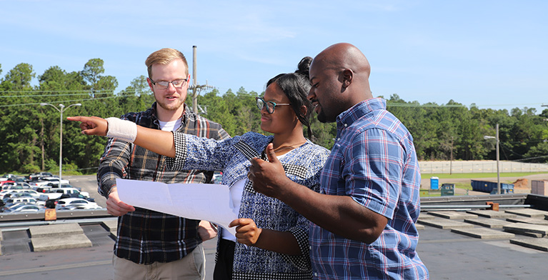 People standing outside, talking, holding paper and pointing