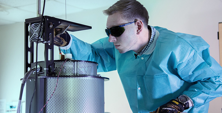 A scientist wearing safety glasses and gloves looking at equipment