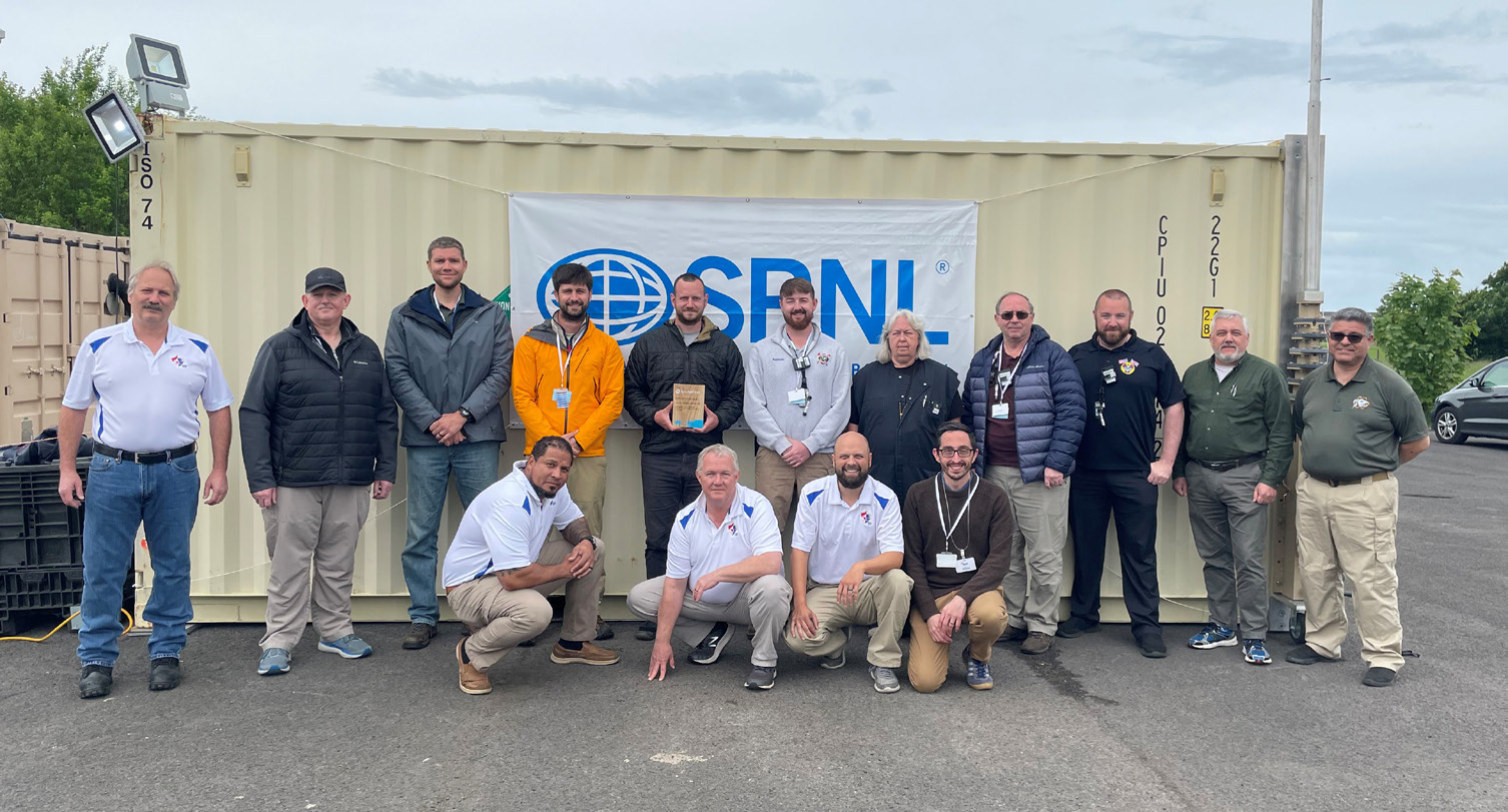 Group of people posing in front of shipping container with SRNL sign attached.