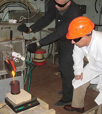 Two engineers adjusting machine as it pour hot melted metals into steel cup