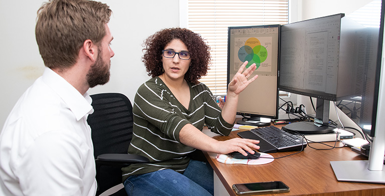 A woman sitting at a computer desk talking to a man