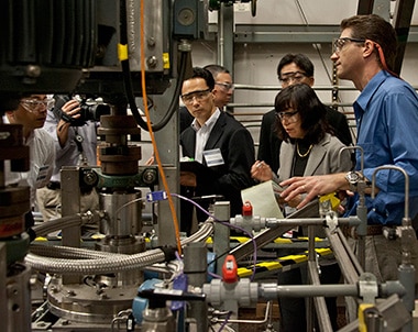 Group of people hovering around a machine while taking notes and conversing with one another