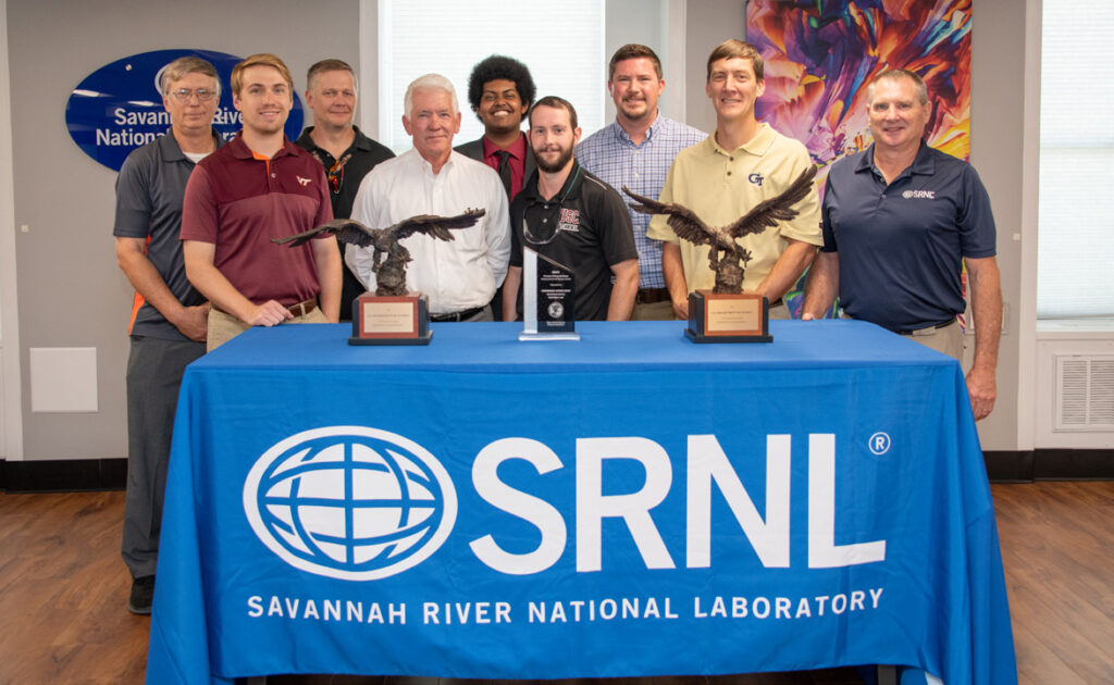 group of people standing behind table with SRNL logo table cloth